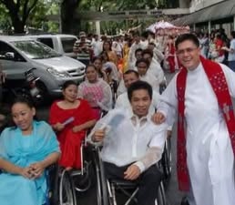 Fr. Arnold Abelardo standing beside a community member using a wheelchair outdoors